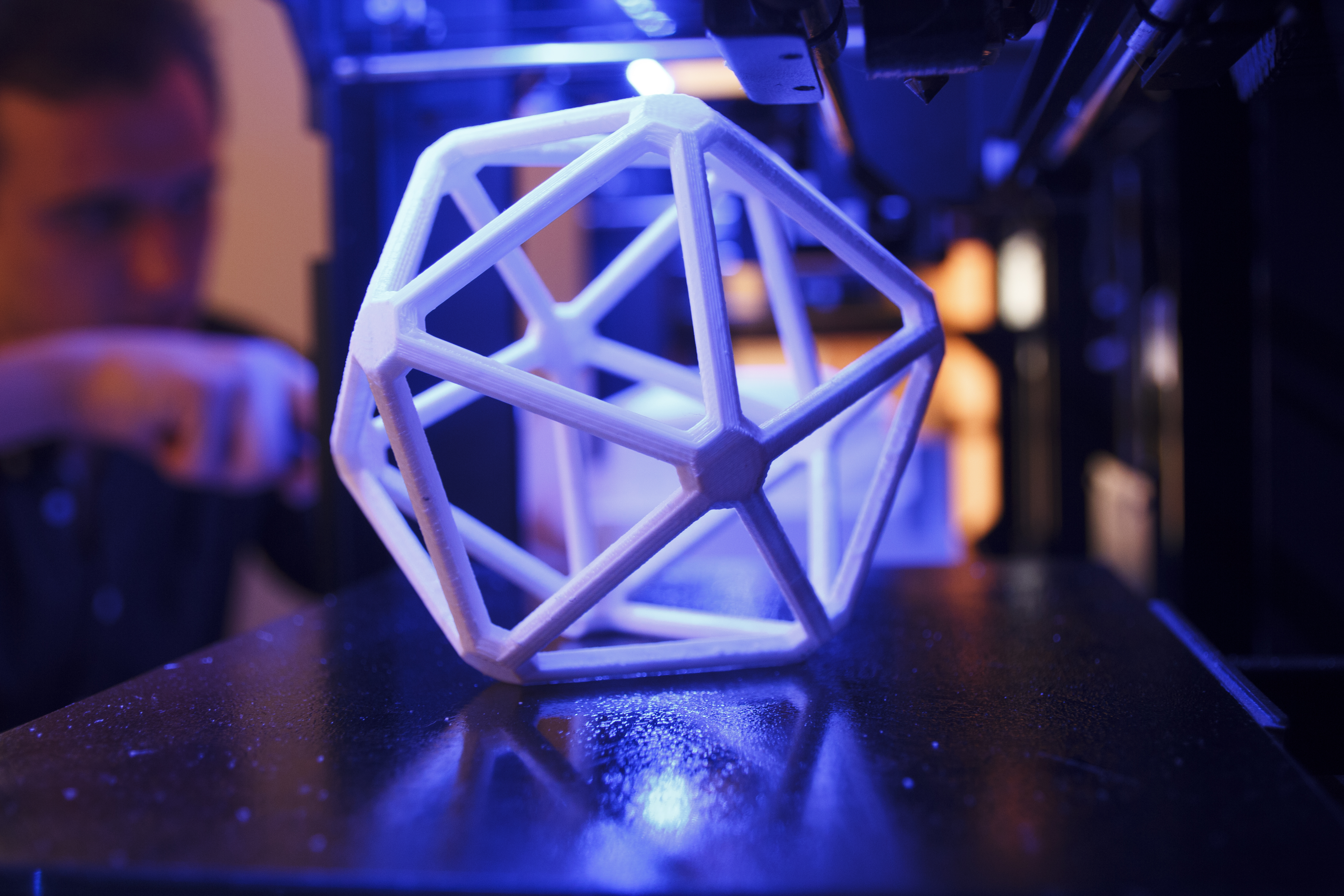 3D geometric figure on the platform of a 3D printer with a man in the background